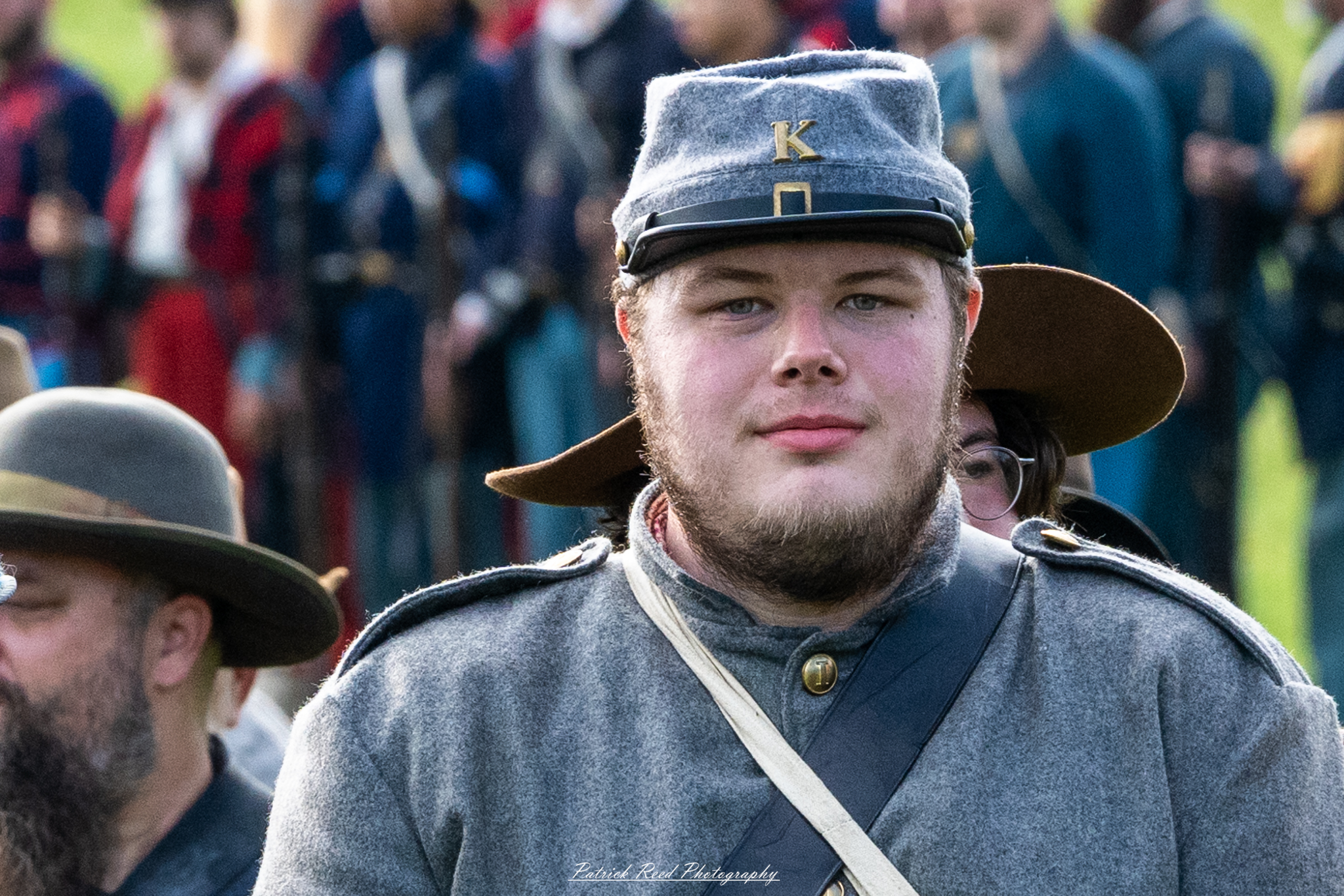 A Confederate soldier standing in ranks, dressed in a gray uniform and holding his weapon at the ready. His posture is straight and disciplined, reflecting the pride and commitment of the troops during the Civil War, as he stands alongside his comrades in formation.
